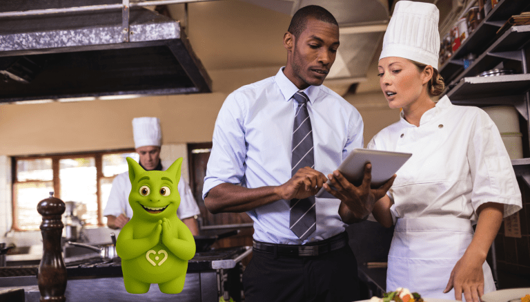 Manager and chef discussing on tablet in kitchen with Tuutuu character smiling beside them.
