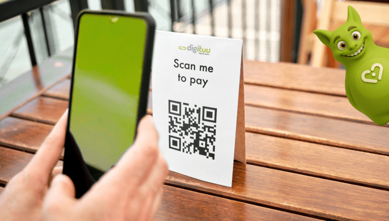 Person scanning QR code to pay via smartphone at a table, with Tuutuu mascot smiling on the side.